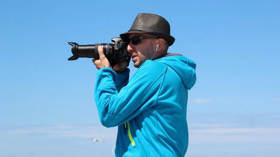 Wildlife photographer adjusting telephoto lens settings in natural outdoor environment during golden hour