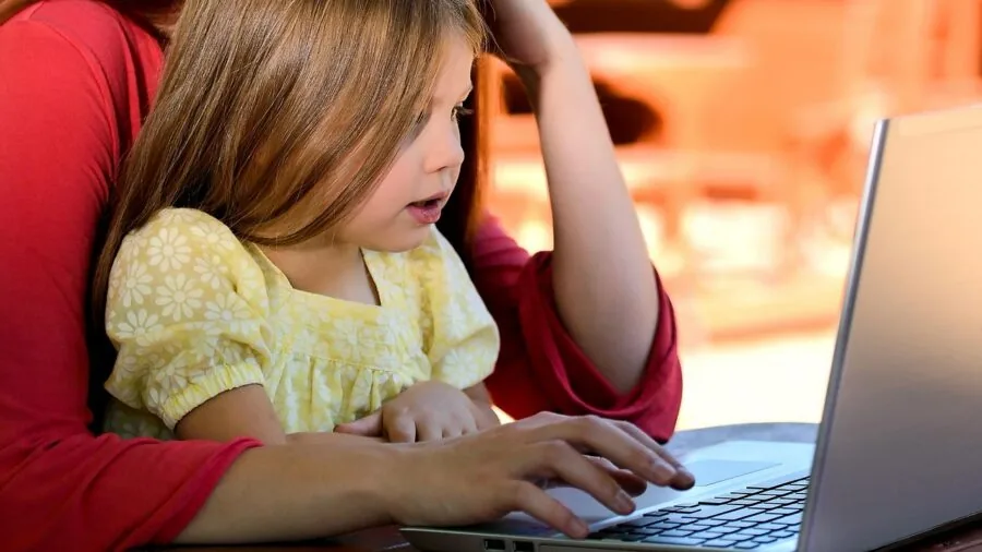 Young child sitting at desk studying laptop screen with concerned expression about device updates