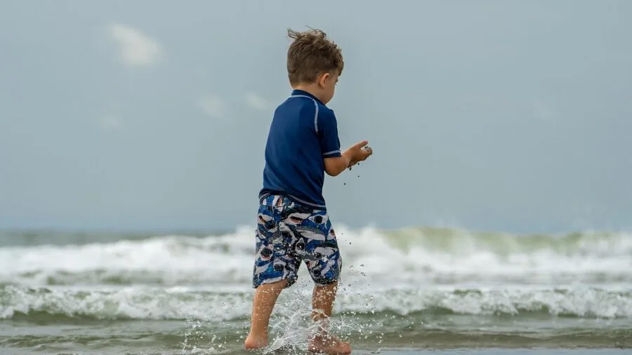 Young child sitting tired on beach sand during daytime outdoor activity