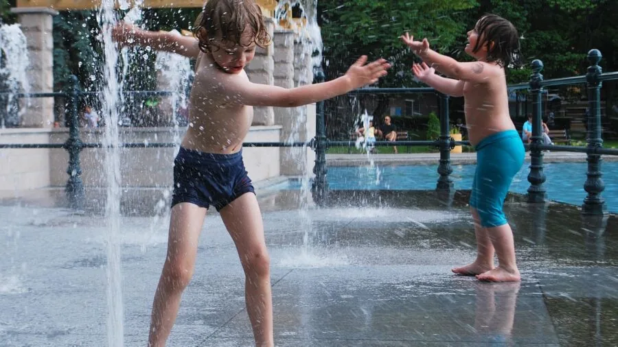 Young child splashing and playing in water outdoors at a park or beach on a sunny day